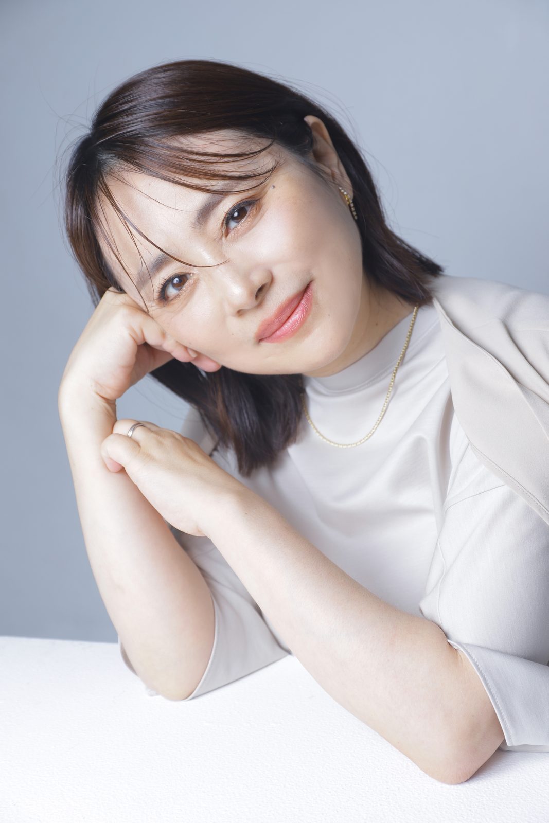 齋藤あづさのポートレート。頬に手を添えて穏やかに微笑んでいる